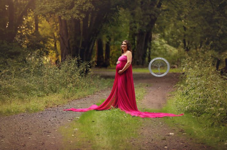 Pregnant woman in red dress stands on a road in the woods