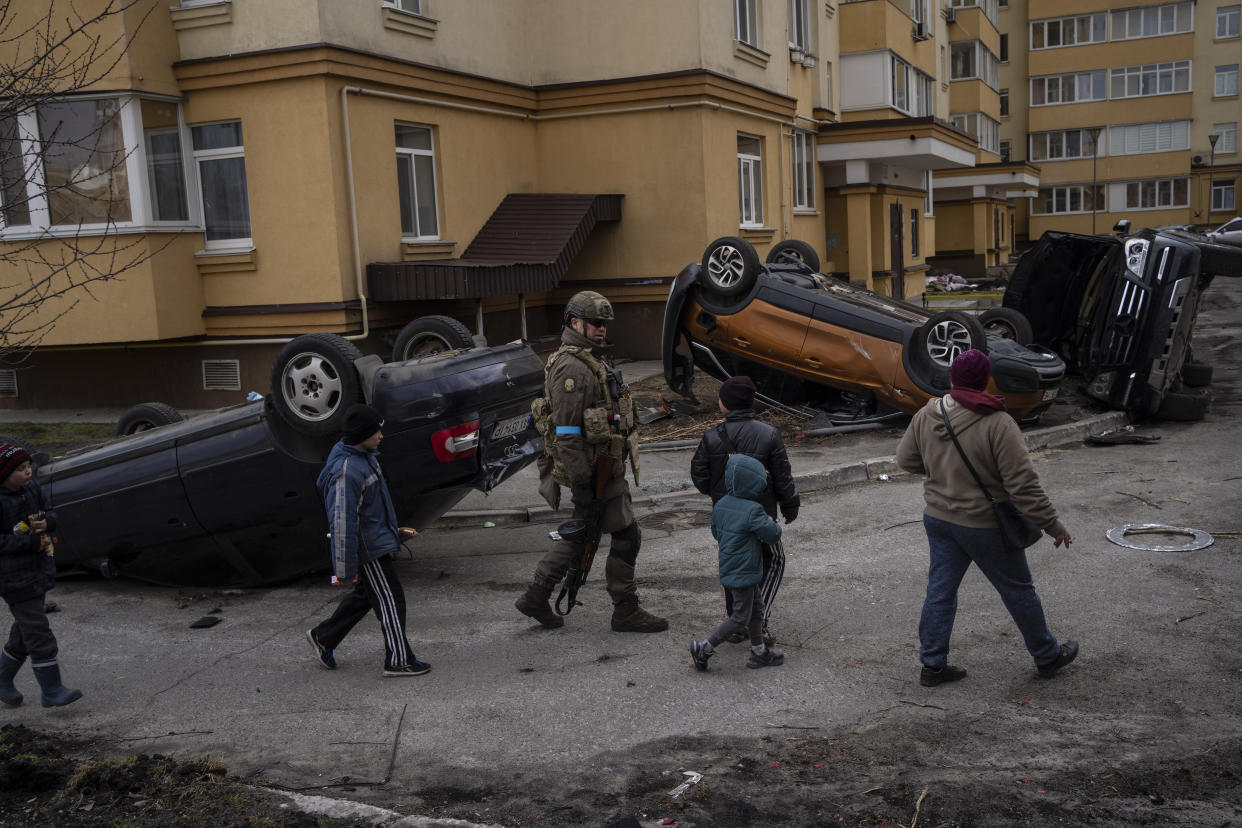 A Ukrainian soldier walks with children passing destroyed cars due to the war against Russia, in Bucha, on the outskirts of Kyiv, Ukraine, Monday, April 4, 2022. (AP Photo/Rodrigo Abd)