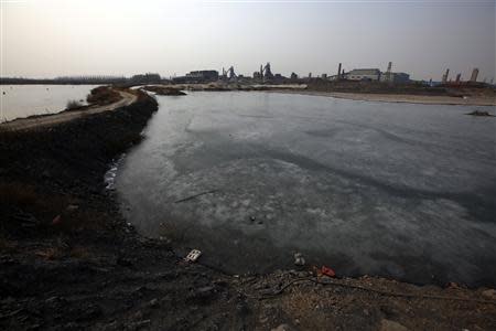 A frozen pond is pictured next to a muddy road near an abandoned steel mill (background) of Qingquan Steel Group in Qianying township, Hebei province February 18, 2014. REUTERS/Petar Kujundzic