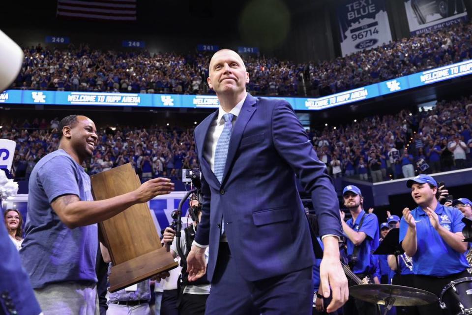 Mark Pope, right, hands off the 1996 national championship trophy to former teammate Derek Anderson before the new Kentucky coach’s introductory press conference at Rupp Arena on Sunday.