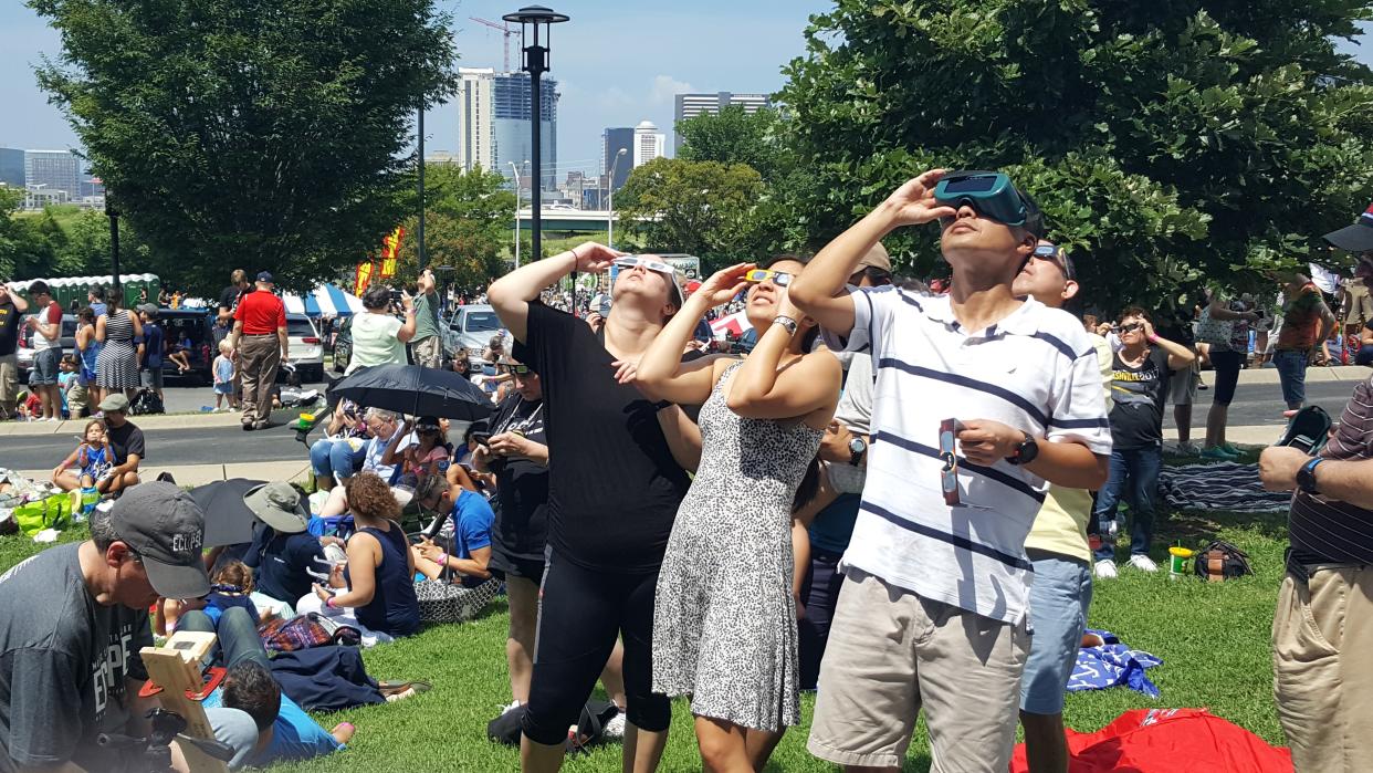  A crowd of people in a city park watch a solar eclipse using safety glasses. 