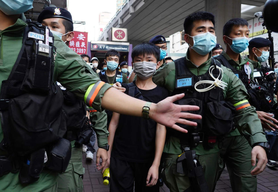 A boy is escorted by police officers to a police van after he walked past the Prince Edward subway station where people tried to place flowers outside and the boy have released soon after, Monday, Aug. 31, 2020 in Hong Kong. Aug. 31 is the first anniversary of police raid on Prince Edward subway station which resulted in widespread images of police beating people and drenching them with pepper spray in subway carriages. (AP Photo/Vincent Yu)