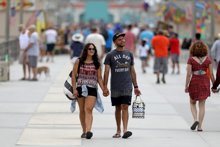 HUNTINGTON BEACH, CA - JUNE 15: People stroll along the pier on Tuesday, June 15, 2021 in Huntington Beach, CA. Restrictions are lifted at most businesses, and Californians fully vaccinated for COVID-19 can go without masks in most settings. (Gary Coronado / Los Angeles Times)