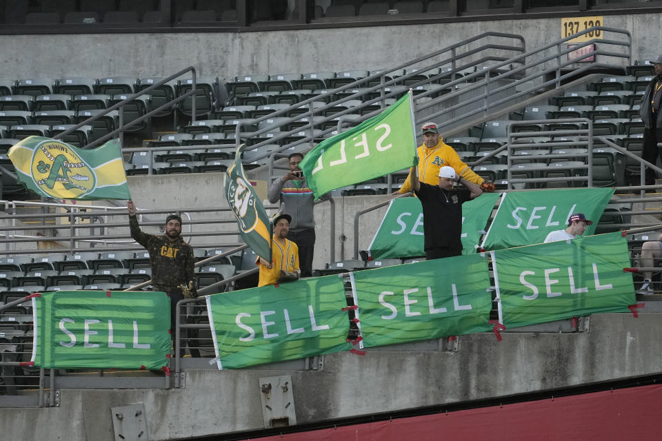 Fans wave flags behind signs calling for Oakland Athletics management to sell the team, during the fourth inning of a baseball game between the Athletics and the Colorado Rockies in Oakland, Calif., Wednesday, May 22, 2024. (AP Photo/Jeff Chiu)