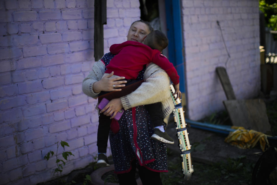 A woman holds a child outside her family's heavily damaged house after a Russian strike in Pokrovsk, eastern Ukraine, Wednesday, May 25, 2022. Two rockets struck the eastern Ukrainian town of Pokrovsk, in the Donetsk region early Wednesday morning, causing at least four injuries. (AP Photo/Francisco Seco)