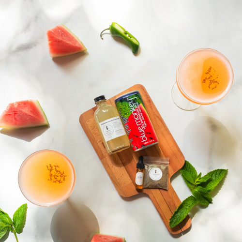 two glasses of margaritas with watermelon, hot peppers, and juice on a wood board