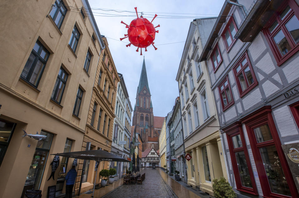 A homemade, luminous representation of the coronavirus hangs above a shopping street in front of the tower of Schwerin Cathedral during the lockdown in Schwerin, Germany, Tuesday, Jan. 5, 2021. A local fishmonger in the almost deserted street built and hung the lantern in the image of the virus. The German Chancellor and the Minister Presidents of the federal states discuss an extension of the lockdown to contain the corona pandemic. (Jens Buettner/dpa via AP)