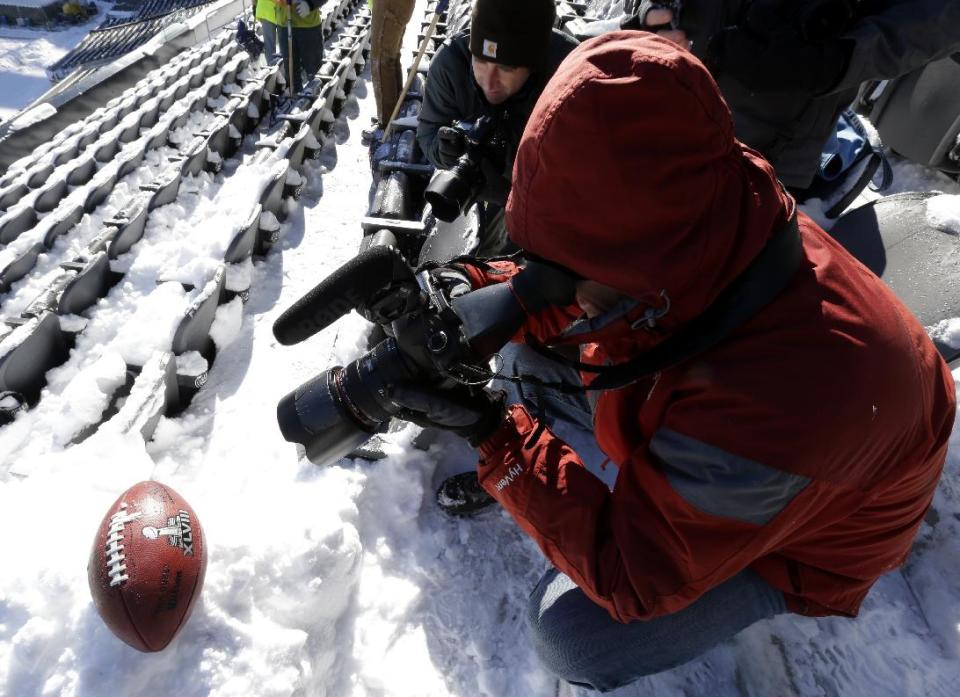 Bergen Record newspaper photographers Tyson Trish, left, and Thomas Franklin, shoot images of a football with the Super Bowl XLVIII logo set on a mound of snow as workers shovel snow off the seating area at MetLife Stadium as crews removed snow ahead of Super Bowl XLVIII following a snow storm, Wednesday, Jan. 22, 2014, in East Rutherford, N.J. Super Bowl XLVIII, which will be played between the Denver Broncos and the Seattle Seahawks on Feb. 2, will be the first NFL title game held outdoors in a city where it snows. (AP Photo/Julio Cortez)