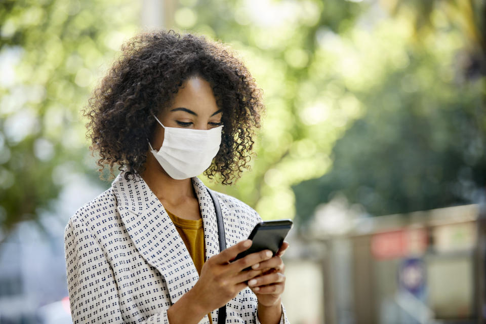 Businesswoman using smart phone in city. Entrepreneur is looking at cell while standing outdoors during pandemic. She is in formals.