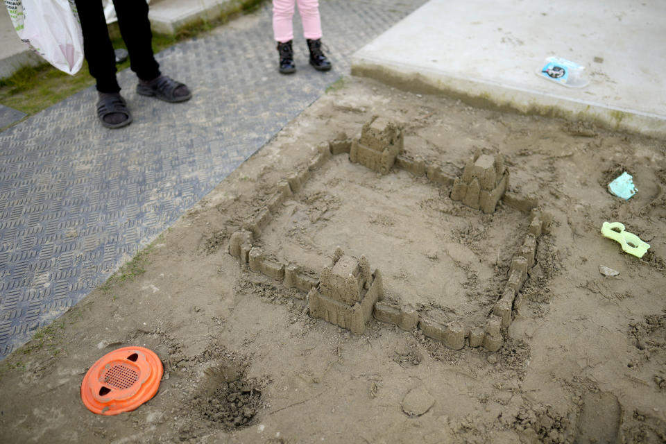 A small girl and her grandmother look at a sandcastle constructed in a makeshift garden at the Ukraine village, which has been constructed for Ukrainian families fleeing the war, in Linkeroever, Belgium, Friday, March 17, 2023. Despite the warm welcome for millions of Ukraine refugees on European Union soil since the Russian invasion, EU officials said Tuesday, June 6, 2023 that there are some fears of wavering support caused by a bad economy hitting poor families especially and the creeping influence of Russian propaganda. (AP Photo/Virginia Mayo)