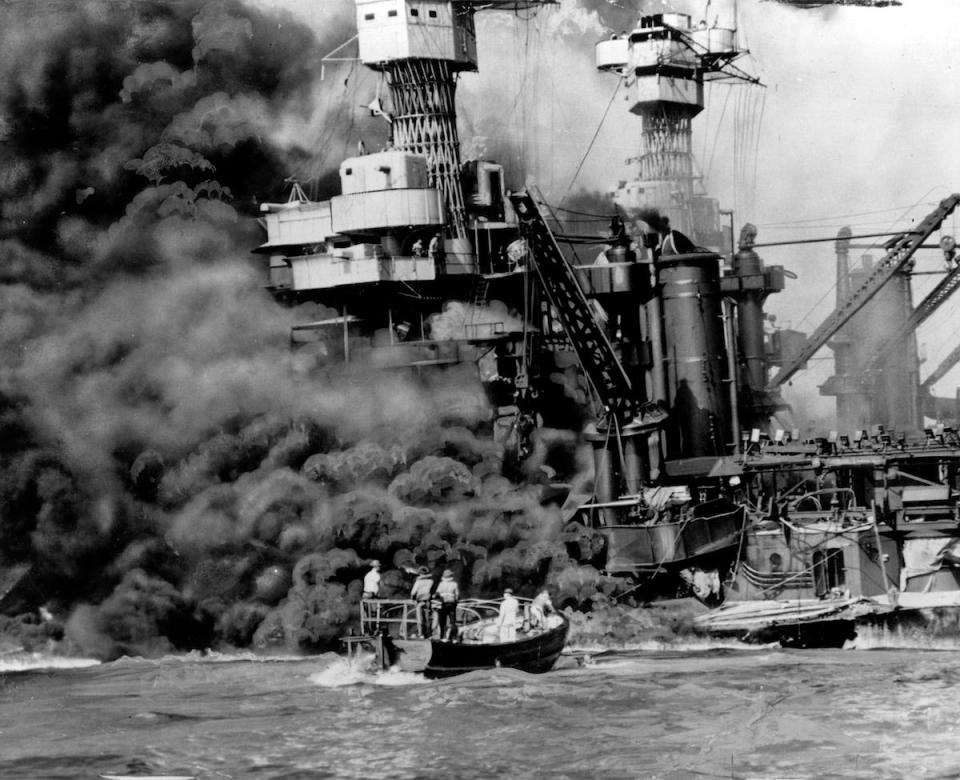 a small boat rescues a crew member from the water as heavy smoke rolls out of the stricken USS West Virginia after the Japanese bombing of Pearl Harbor, Hawaii. Two men can be seen on the superstructure, upper center. The mast of the USS Tennessee is beyond the burning West Virginia. Saturday marks the 72nd anniversary of the attack that brought the United States into World War II.