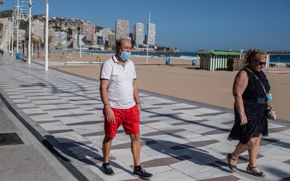 Two people wearing a face masks walk along the promenade of the closed Playa de Levante Beach in Benidorm, Spain, on May 11, 2020 - David Ramos/Getty Images