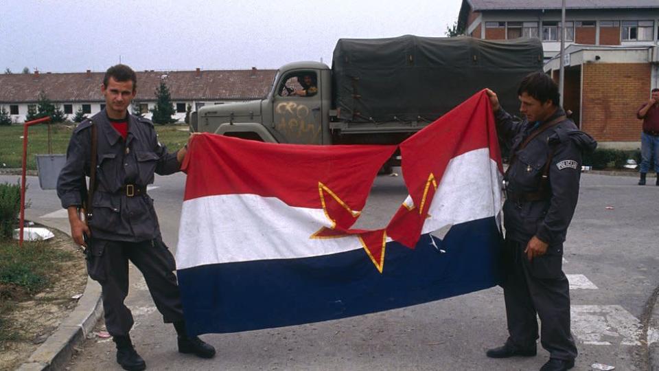 Hombres sosteniendo una bandera yugoslava rota.