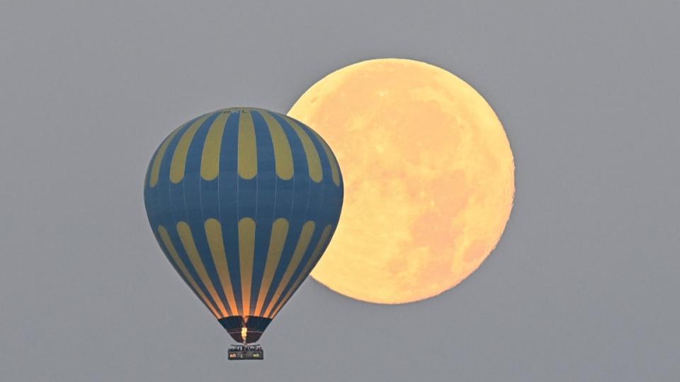     A close-up of a blue hot air balloon and the full moon. 