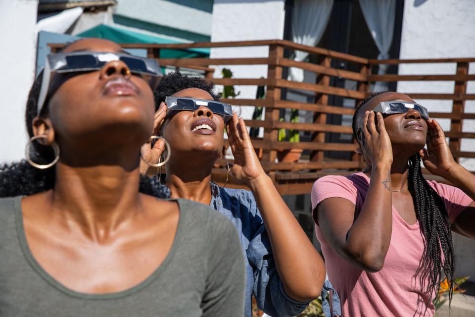 three women friends at home enjoying solar eclipse looking at the sun with solar eclipse glasses