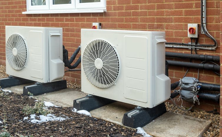 Two large white boxes with fans attached to the exterior wall of a building.