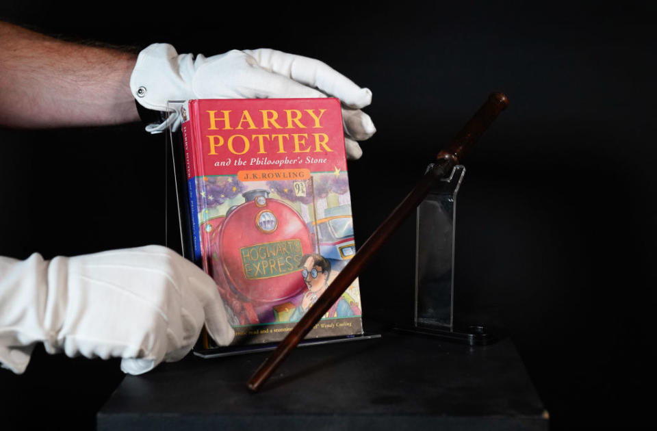 Someone with gloved hands carefully placing an edition of Harry Potter and the Philosopher's Stone next to a wand