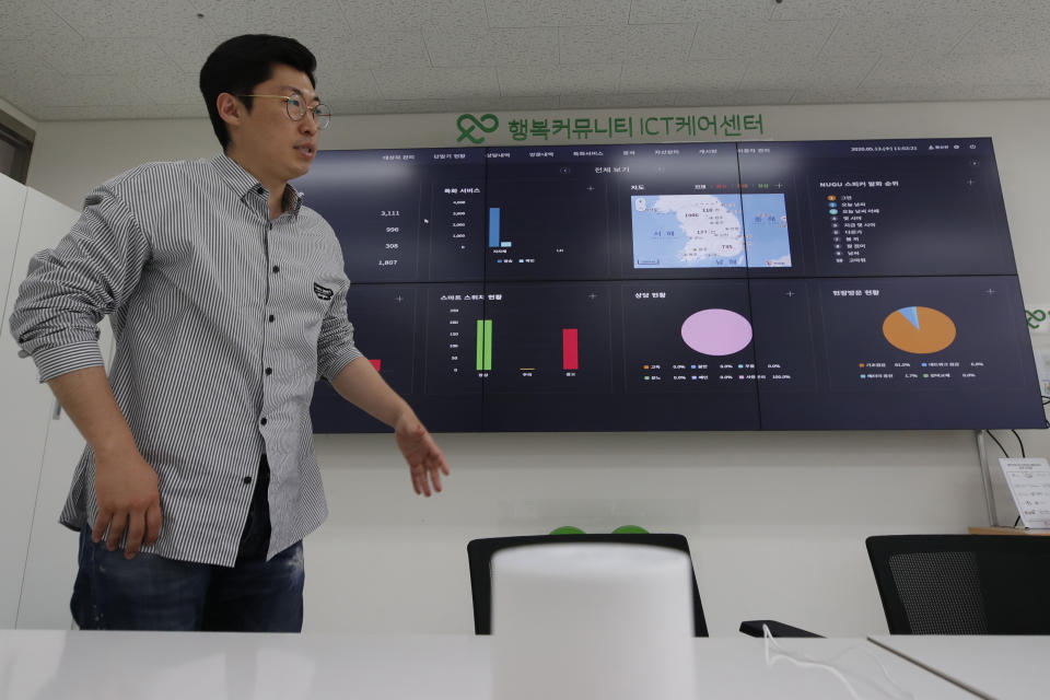 Hwang Seungwon, director of a social enterprise established by SK Telecom to handle the service, speaks in front of an electronic dashboard during an interview in Seoul, South Korea, May 13, 2020. Hwang points a remote control toward a huge NASA-like overhead screen stretching across one of the walls. With each flick of the control, a colorful array of pie charts, graphs and maps reveals the search habits of thousands of South Korean senior citizens being monitored by voice-enabled “smart” speakers, an experimental remote care service the company says is increasingly needed during the coronavirus crisis. (AP Photo/Lee Jin-man)