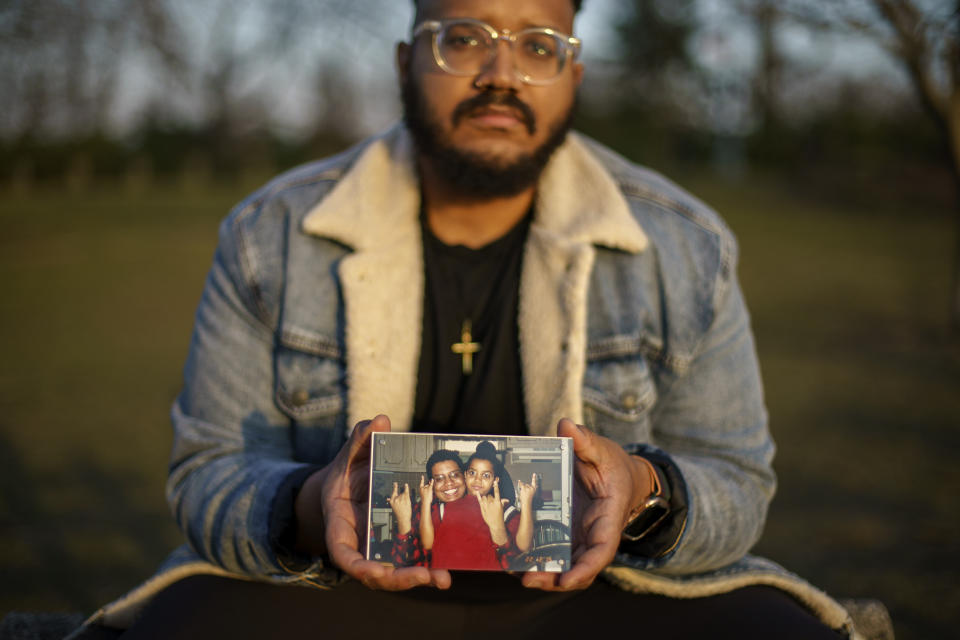 FILE - Adam Almonte holds a photo of him with his older brother, Fernando Morales, on a bench where they used to sit and eat tuna sandwiches after playing catch in Fort Tryon Park in New York, Wednesday, March 16, 2022. Morales died April 7, 2020 from COVID-19 at age 43. After a weekend of gun violence in America, Saturday, May 14, 2022, when shootings killed and wounded people grocery shopping, going to church and simply living their lives, the nation marked a milestone of 1 million deaths from COVID-19. The number, once unthinkable, is now a pedestrian reality in the United States, just as is the reality of the continuing epidemic of gun violence that kills tens of thousands of people a year. (AP Photo/David Goldman, File)