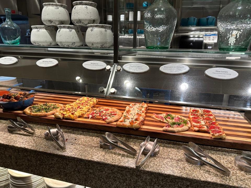A variety of pizzas on display at the Bacchanal buffet with tongs in front of each