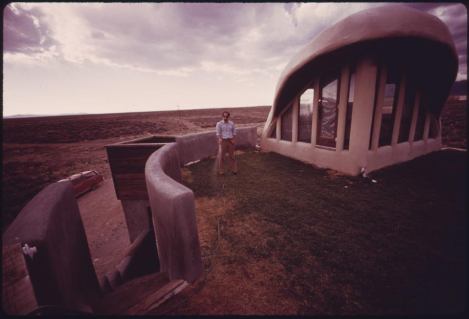 Architect and experimental house builder Michael Reynolds who used a variety of recycled materials to complete his first experimental home near Taos in 1974. Owned by lawyer Steve Natelson, shown in the picture, the home had a lawn on the roof, a common feature of sustainable design today, but an unusual concept for homes at the time. This experimental lawn required daily attention because of the dry environment.