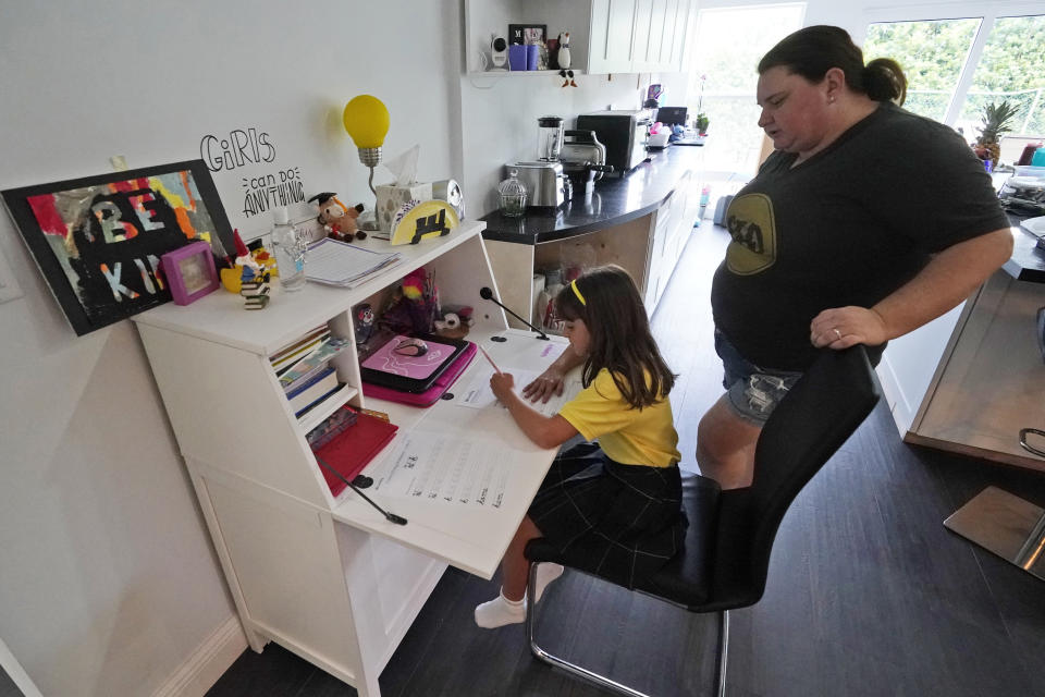 Erica Chao, right, watches her daughter Emily work on a writing exercise, Thursday, Oct. 1, 2020, at their home in North Miami Beach, Fla. Rather than wait to see how the Miami-Dade school system would handle instruction this fall, Erica Chao enrolled her two daughters in a private school that seemed better positioned to provide remote learning than their public elementary school was when the coronavirus first reached Florida. (AP Photo/Wilfredo Lee)