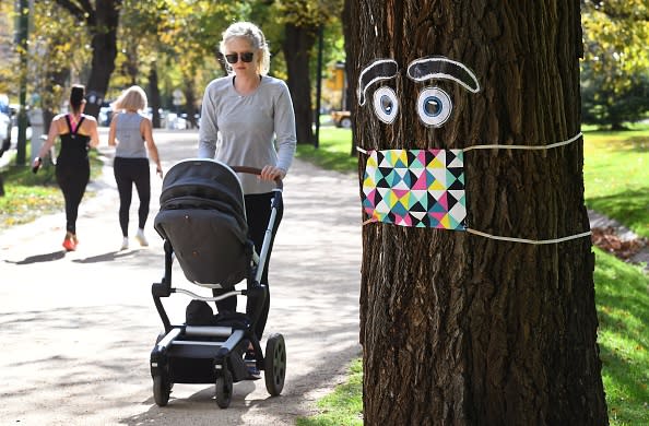 A woman pushes a pram past a giant mask and eye display stuck to a tree in Melbourne.