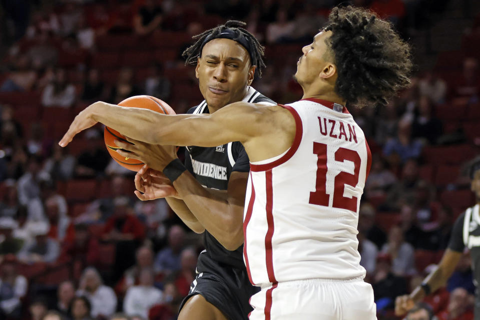 Providence forward Rafael Castro, left, tries to keep control of the ball as Oklahoma guard Milos Uzan (12) defends during the first half of an NCAA college basketball game, Tuesday, Dec. 5, 2023, in Norman, Okla. (AP Photo/Nate Billings)