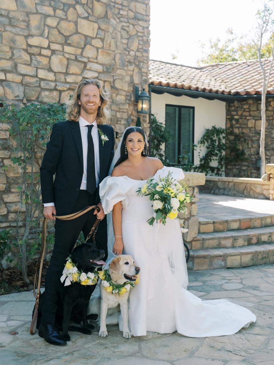 A bride and groom pose with a black dog and a yellow dog on their wedding day.