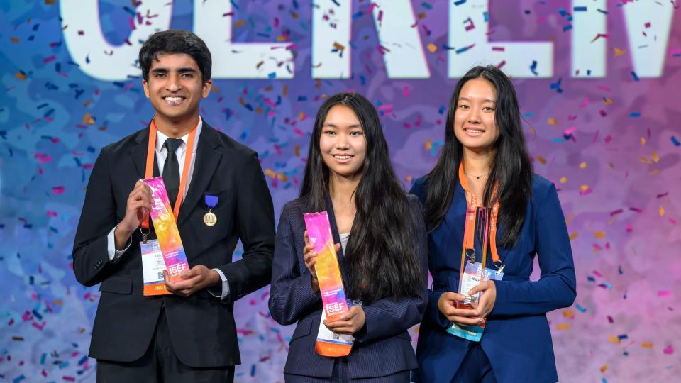 Three students in suits holding ISEF awards with confetti raining down around them