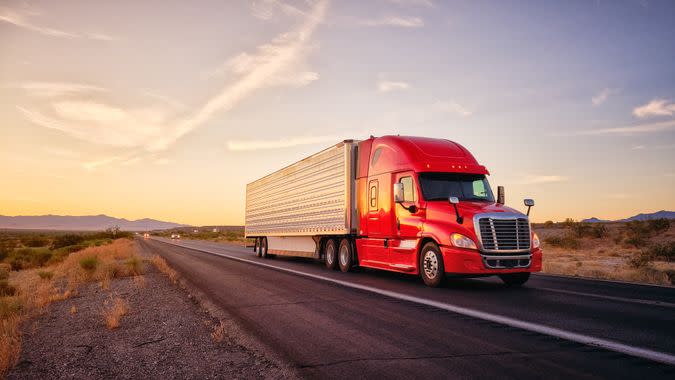 Large semi truck hauling freight on the open highway in the western USA under an evening sky.