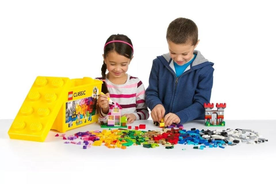 Two child models playing with a table full of colorful Lego bricks