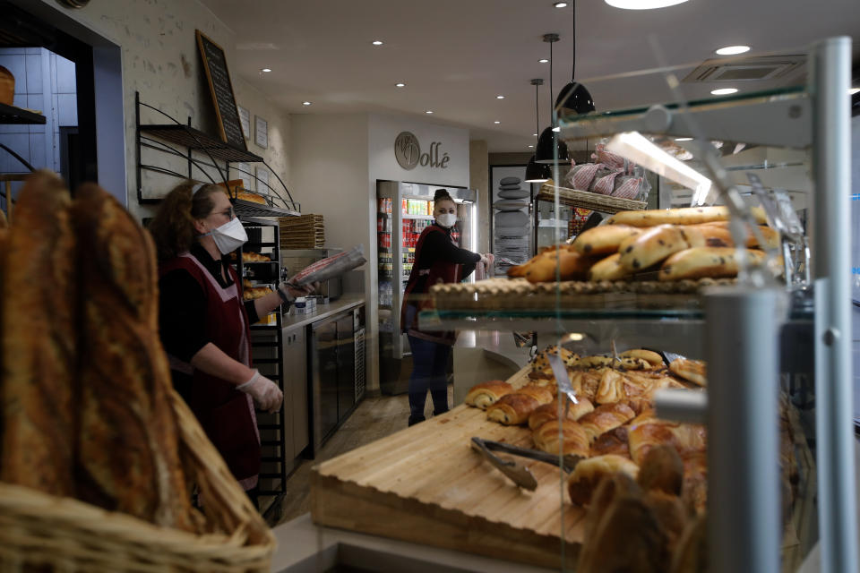 Bakers sell bread in a Boulogne Billancourt bakery, outside Paris, Tuesday, March 24, 2020. French President Emmanuel Macron urged employees to keep working in supermarkets, production sites and other businesses that need to keep running amid stringent restrictions of movement due to the rapid spreading of the new coronavirus in the country. For most people, the new coronavirus causes only mild or moderate symptoms. For some it can cause more severe illness, especially in older adults and people with existing health problems. (AP Photo/Christophe Ena)