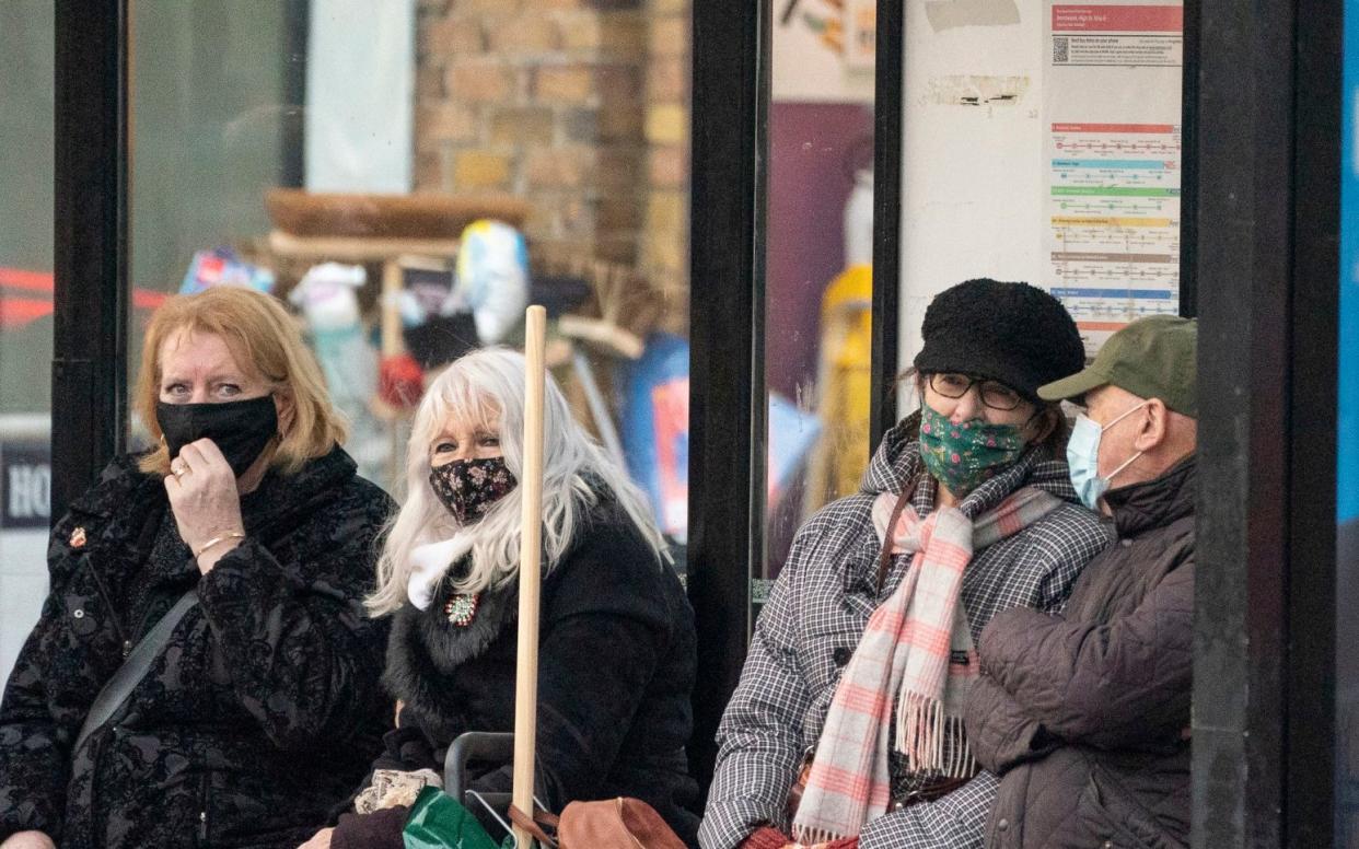 People wear face coverings at a bus stop in Brentwood, Essex, as cases of the omicron variant are confirmed across the country - Dominic Lipinski /PA