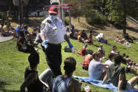 FILE - San Francisco Police Auxiliary Law Enforcement Response Team (ALERT) volunteer David Flynn offers face masks to help prevent the spread of the coronavirus at Dolores Park in San Francisco, Sunday, May 24, 2020. California is creating roving "strike teams" drawn from seven state agencies that will enforce state guidelines designed to slow the spread of the coronavirus, Gov. Gavin Newsom said Wednesday, July, 1, 2020. The teams include representatives from the California Highway Patrol; the Division of Occupational Safety and Health, known as CalOSHA; the Department of Alcohol Beverage Control; the Board of Barbering & Cosmetology; the departments of Business Oversight and Consumer Affairs. (AP Photo/Jeff Chiu, File)