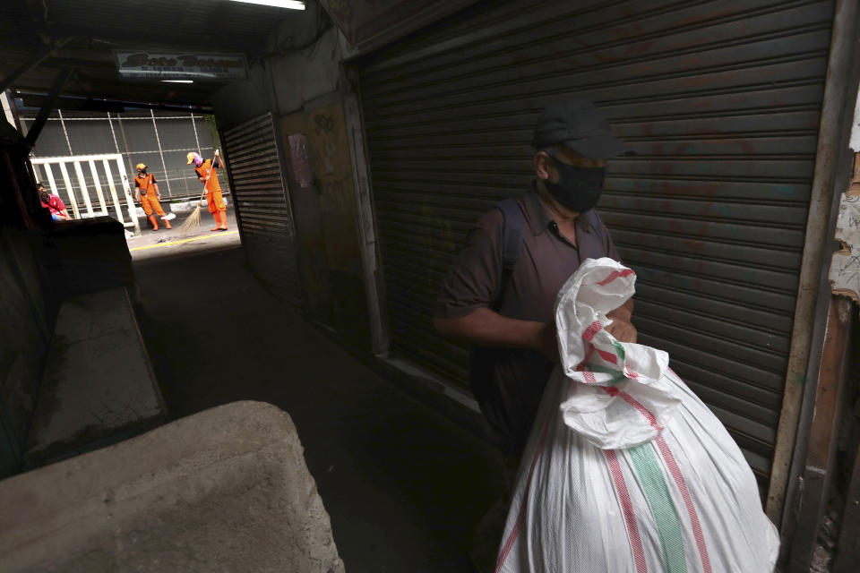 In this Thursday, April 30, 2020, photo, a man walks past closed shops as municipal workers sweep a sidewalk at Tanah Abang textile market that is shut down due to the new coronavirus outbreak in Jakarta, Indonesia. May Day usually brings both protest rallies and celebrations rallies marking international Labor Day. This year it's a bitter reminder of how much has been lost for the millions left idle or thrown out of work due to the coronavirus pandemic. Garment workers in Asia are among the hardest hit as orders dry up and shutdowns leave factories shuttered. (AP Photo/Tatan Syuflana)