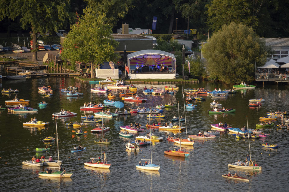 The Staatsphilharmonie plays a concert on the lake stage on the Gro'er Dutzendteich in front of spectators who watch the concert on their own boats, Saturday, Aug. 1, 2020, in Nuremberg, Germany. Due to the musical events Bardentreffen, Klassik Open Air and Stars in Luitpoldhain, which were cancelled due to the coronavirus, the project office in the Culture Division of the City of Nuremberg has organized three different concerts with an open-air concert weekend on the banks of the Dutzendteich. (Daniel Karmann/dpa via AP)