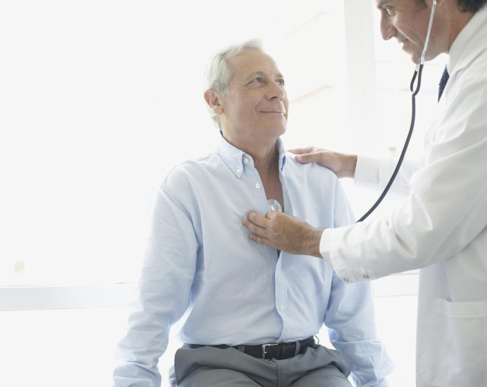 A doctor holds a stethoscope over the chest of an older male patient.