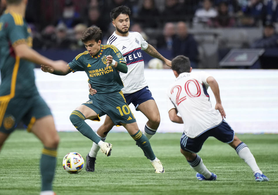 LA Galaxy's Riqui Puig (10) evades Vancouver Whitecaps' Ryan Raposo, back, and Andres Cubas (20) during the first half of an MLS soccer match Saturday, April 13, 2024, in Vancouver, British Columbia. (Darryl Dyck/The Canadian Press via AP)