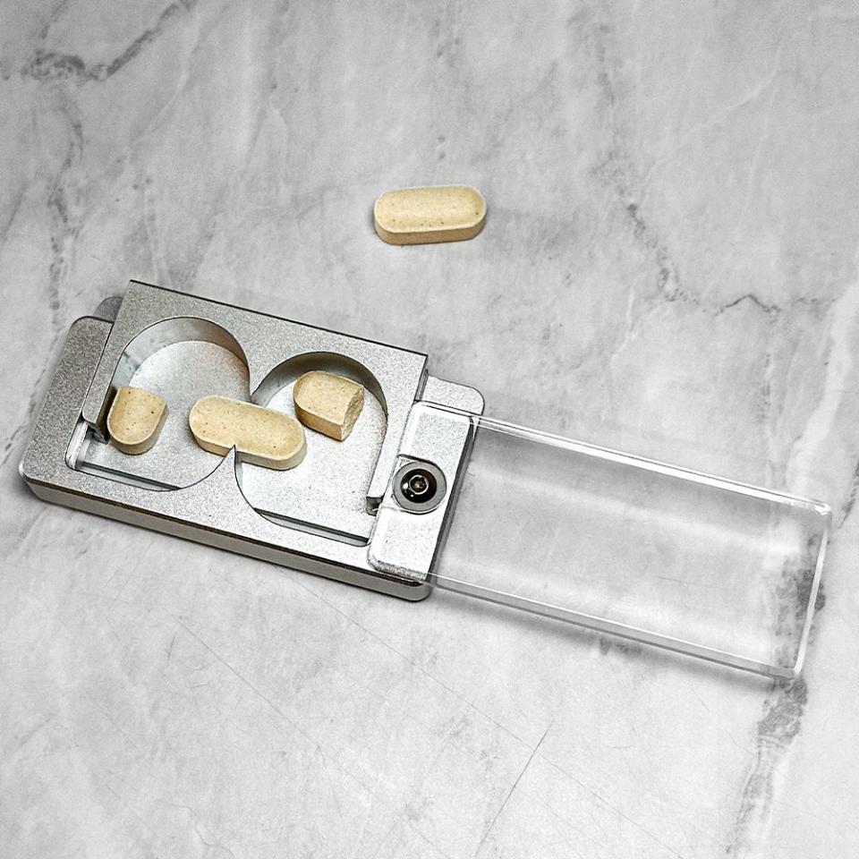 equalpill pill splitter with a a pill split in half in either side, and a whole pill in the middle where the sharp cutter is