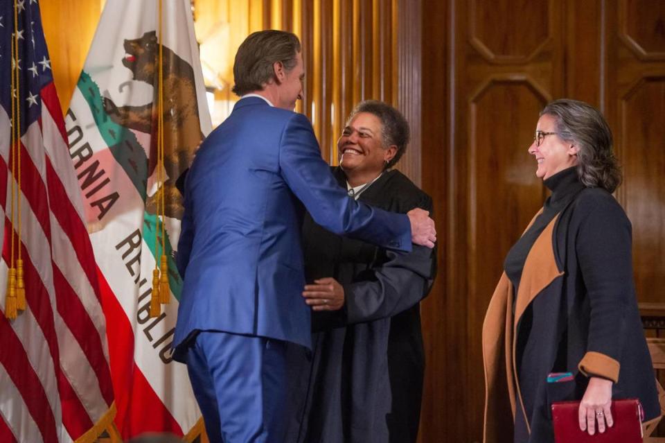 Governor Gavin Newsom hugs new Associate Justice Kelli Evans while her spouse Terri Shaw, right, watches after the swearing-in Monday.