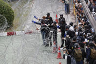 Protesters try to get through barbed wire barricading the base entrance of the 11th Infantry Regiment, a palace security unit under direct command of the Thai king, Sunday, Nov. 29, 2020 in Bangkok, Thailand. Pro-democracy demonstrators are continuing their protests calling for the government to step down and reforms to the constitution and the monarchy, despite legal charges being filed against them and the possibility of violence from their opponents or a military crackdown. (AP Photo/Sakchai Lalit)