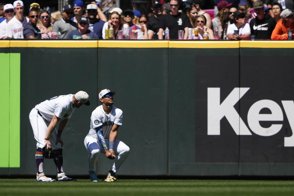 Seattle Mariners left fielder Luke Raley, left, checks on center fielder Julio Rodríguez, right, holds his wrist after falling while catching a fly ball hit by Baltimore Orioles' Jordan Westburg during the sixth inning of a baseball game Thursday, July 4, 2024, in Seattle. (AP Photo/Lindsey Wasson)