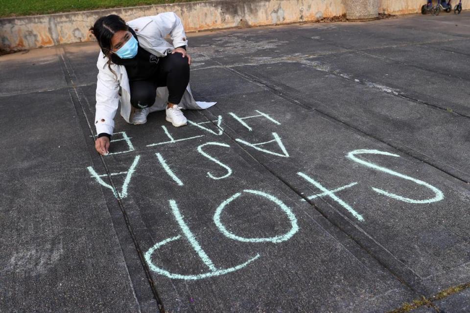 An organizer of the Asian Solidarity Candlelight Vigil writes “Stop Asia Hate” on the sidewalk before the event at Marshall Park in Charlotte, N.C., on Sunday, March 21, 2021.
