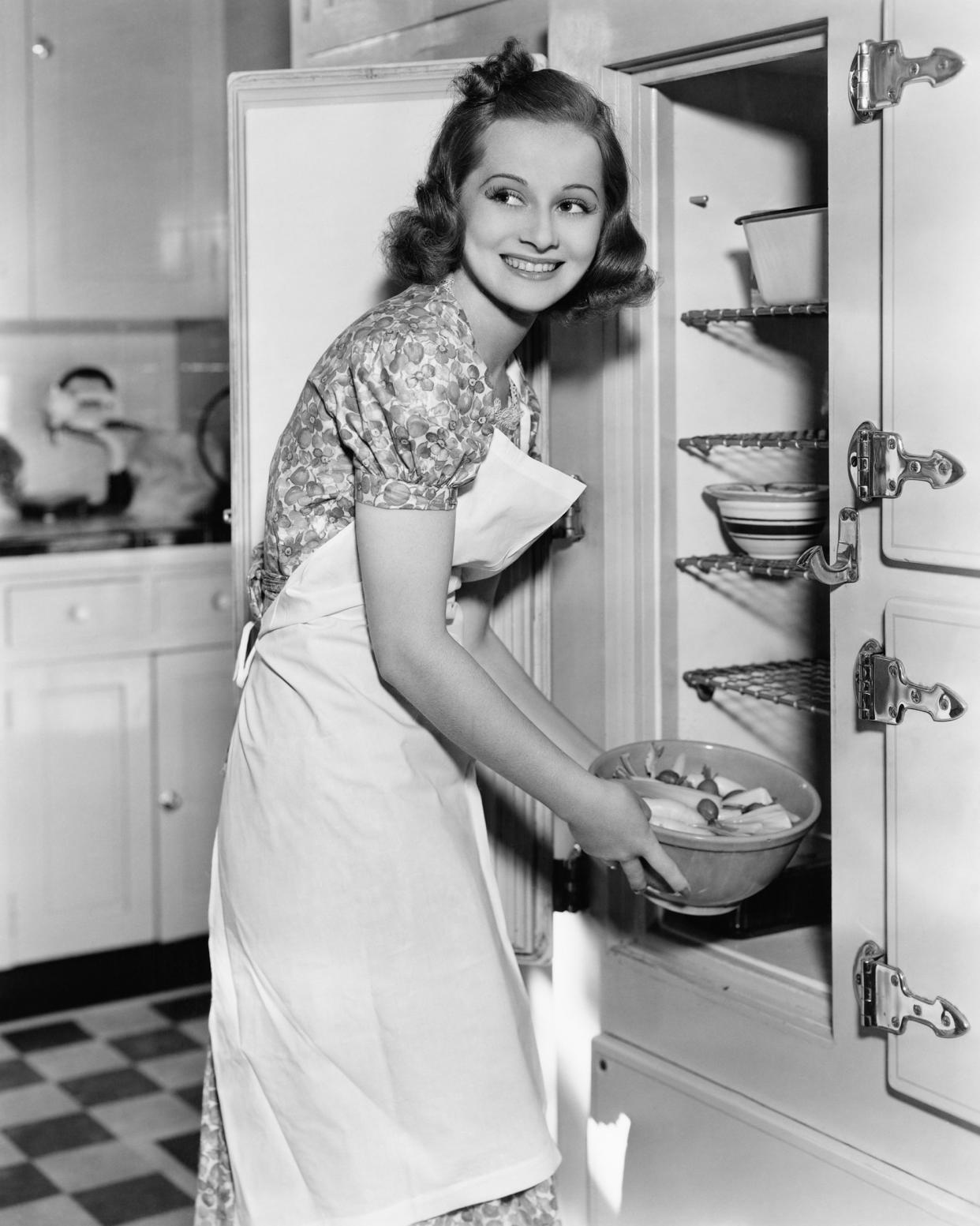 young woman in an apron in her kitchen taking food out of the refrigerator