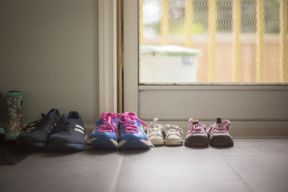Four pairs of shoes by a door, including adult sneakers, child's shoes, reflecting a family's daily life