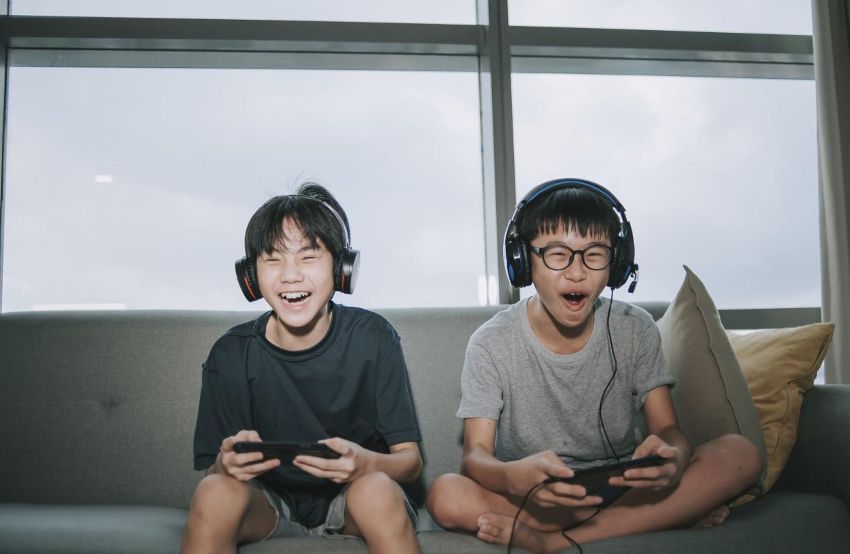 2 asian chinese sibling brother sitting on sofa playing online video games with headset in living room during weekend