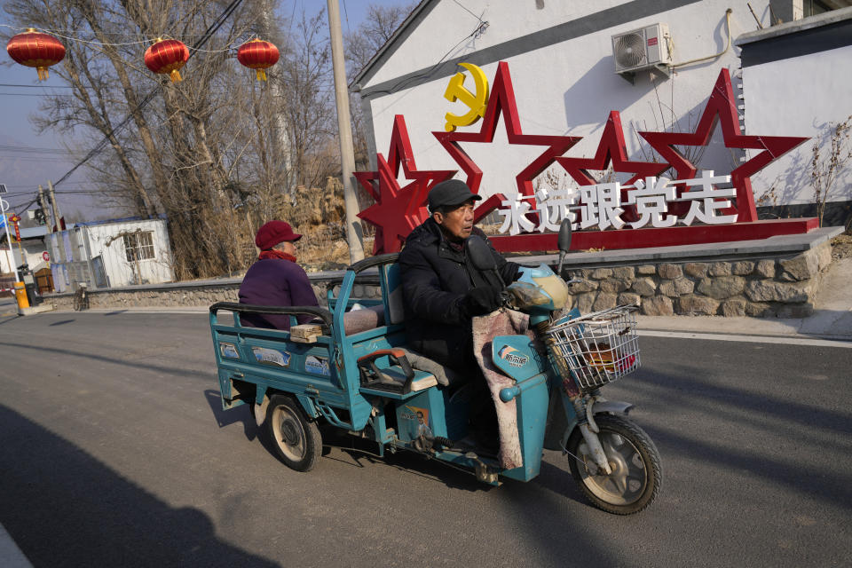 Local residents past by a sign which reads "Forever follow the Communist Party" at Houheilong Miao, a village in Yanqing on the outskirts of Beijing, China, Wednesday, Jan. 5, 2022. The village has a view of the Olympics skiing venue in the distance. Its 20 mostly vacant traditional courtyard houses have been turned into lodgings and a cafe dubbed the "Winter Olympic Home." (AP Photo/Ng Han Guan)