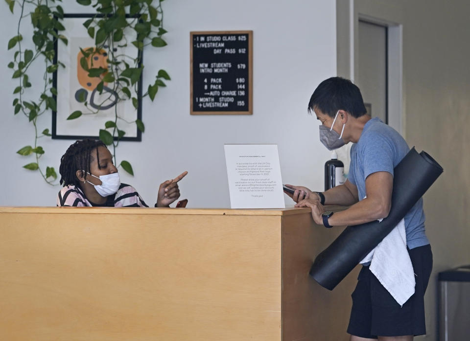 Erica Adamson, left, verifies a mobile digital COVID-19 Vaccine Record on Tony Lai's iPhone at the Highland Park Yoga in Los Angeles, Saturday, Nov. 6, 2021. A vaccine mandate that is among the strictest in the country takes effect Monday, Nov. 8, in Los Angeles, requiring proof of shots for everyone entering a wide variety of businesses from restaurants to shopping malls and theaters to nail and hair salons. (AP Photo/Damian Dovarganes)