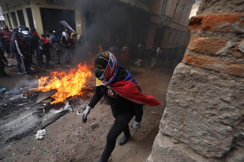 An anti-government demonstrator walks past a barricade in clashes with police during a nationwide strike march against President Lenin Moreno and his economic policies, in Quito, Ecuador, Wednesday, Oct. 9, 2019. Ecuador's military has warned people who plan to participate in a national strike over fuel price hikes to avoid acts of violence, saying it will enforce order. (AP Photo/Fernando Vergara)